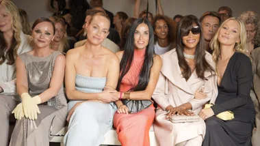 Group of women sitting at a fashion event, smiling. Some wearing elegant dresses and accessories.