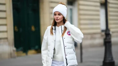 Young woman in a white winter outfit and beanie walking on a city street.