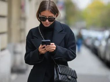 woman wearing black walks down street texting