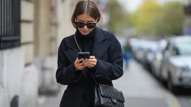 woman wearing black walks down street texting