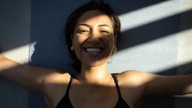 Woman smiling as she lies on her back in shadows.