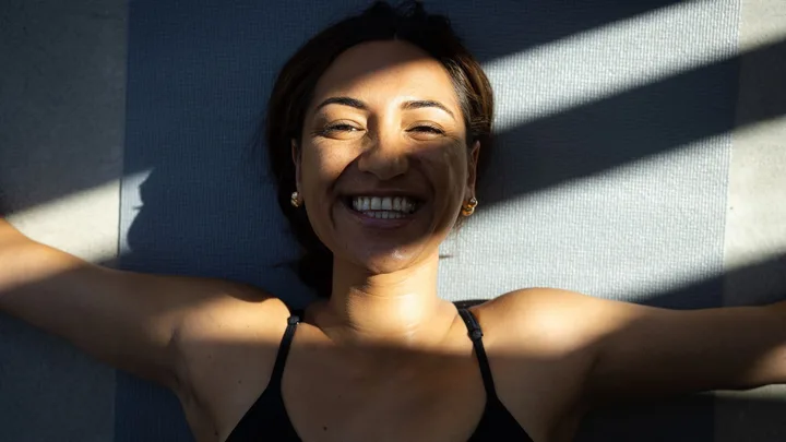 Woman smiling as she lies on her back in shadows.