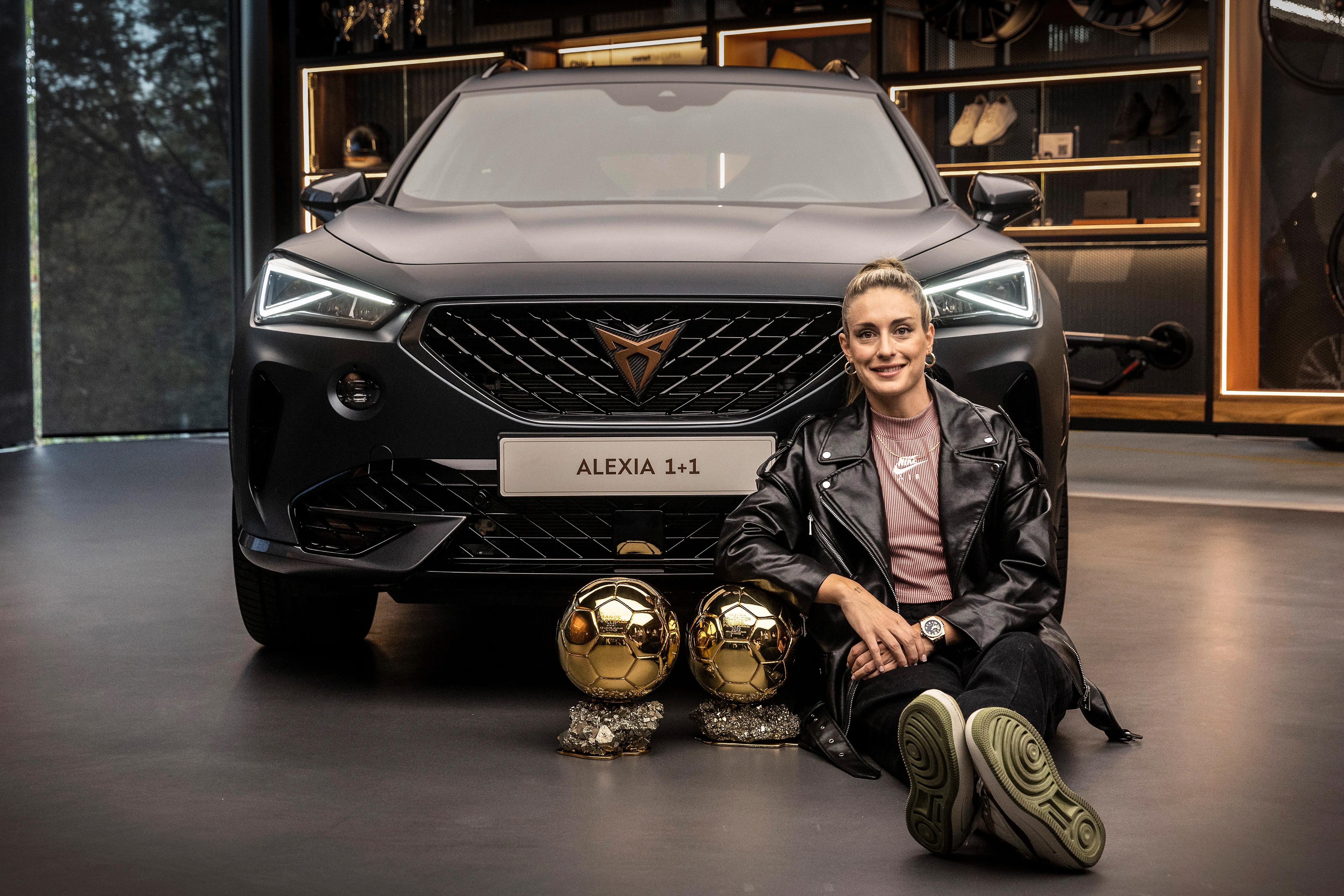 Alexia Putellas with her FIFA trophies sitting in front of a CUPRA car.