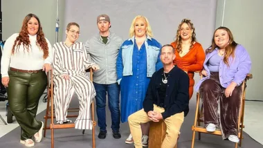A group of seven people posed together in a studio setting, with some sitting and others standing.