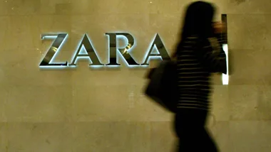 A person walking past a Zara store logo on a beige wall.