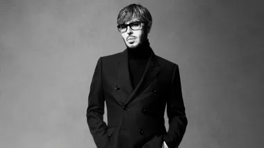 Man in black blazer and turtleneck, wearing glasses, in a black and white portrait.