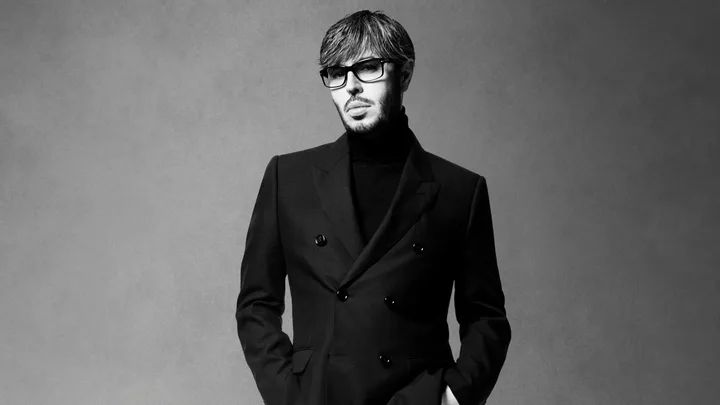 Man in black blazer and turtleneck, wearing glasses, in a black and white portrait.