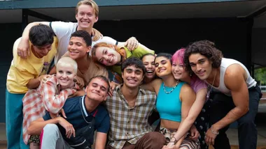 Group of diverse young adults smiling and hugging in a casual outdoor setting.