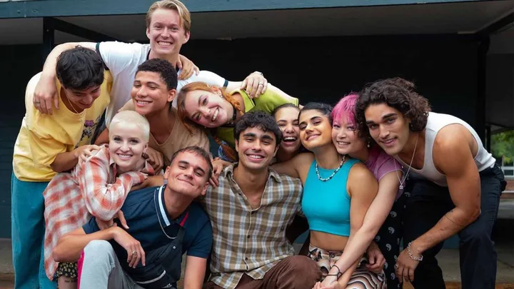 Group of diverse young adults smiling and hugging in a casual outdoor setting.