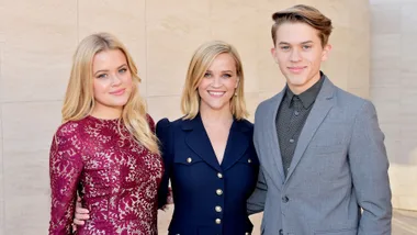 Three people posing together, with one in a burgundy dress, one in a navy outfit, and the other in a gray suit.