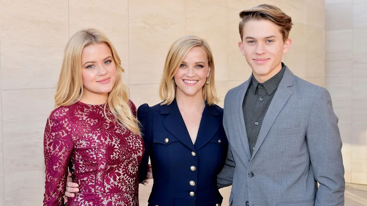 Three people posing together, with one in a burgundy dress, one in a navy outfit, and the other in a gray suit.