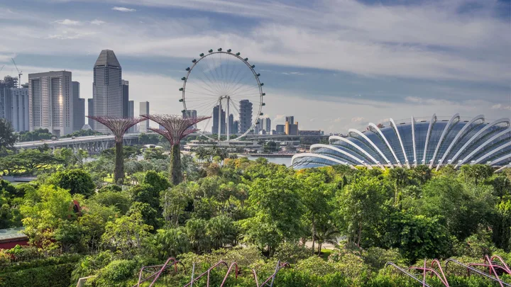 A scenic view of Singapore's skyline, featuring the Supertrees, Ferris wheel, and glass-domed conservatories.