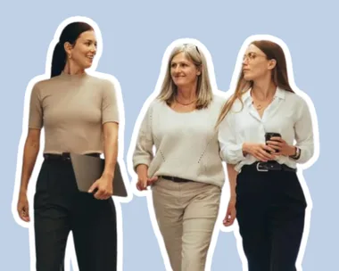 Three women walking and talking, one holding a laptop, another a smartphone, on a light blue background.