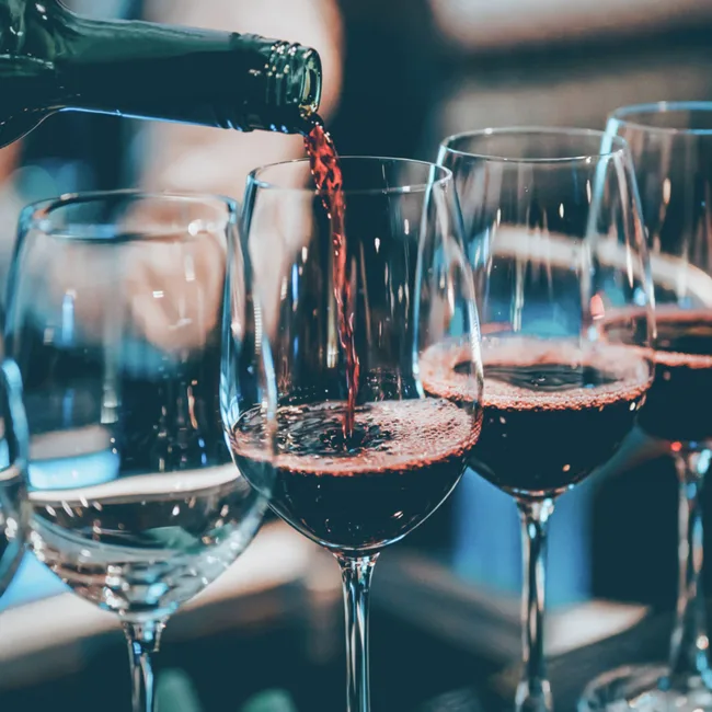 Red wine being poured into several glasses in a dimly lit setting.