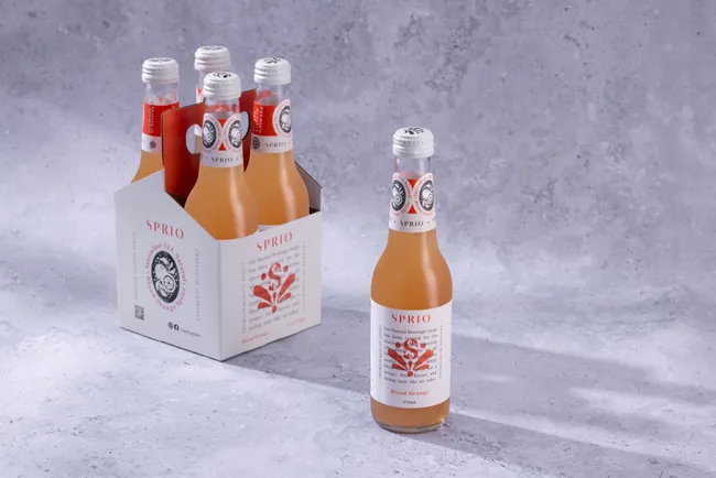 Pack of four "Sprio" blood orange bottles with one bottle placed in front on a textured gray background.