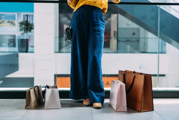 A person in blue pants and a yellow top holding shopping bags in a mall.