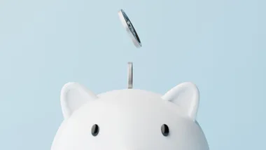 A coin being dropped into a white piggy bank against a light blue background.