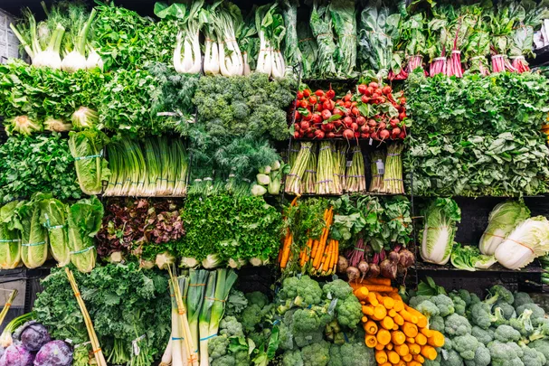 A variety of fresh vegetables displayed on shelves, including broccoli, carrots, lettuce, and radishes.