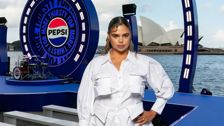Person in a white outfit stands in front of a Pepsi stage by the Sydney Opera House.