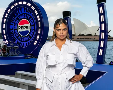 Person in a white outfit stands in front of a Pepsi stage by the Sydney Opera House.