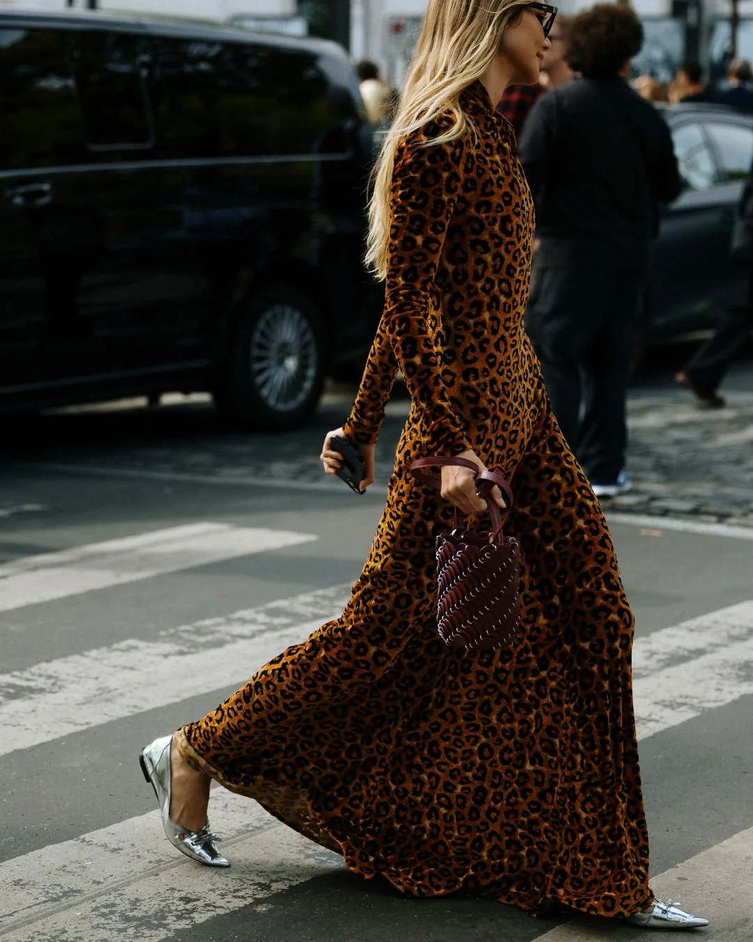 A woman wearing a floor length long sleeve leopard print velvet gown. 