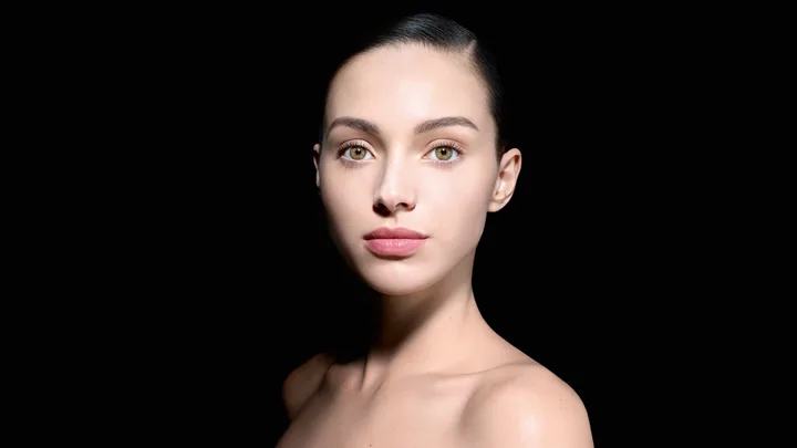 Portrait of a woman with slicked-back hair against a black background, showcasing clear skin and neutral expression.