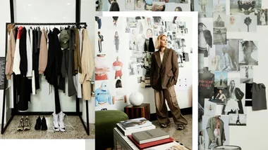 Fashion designer in oversized suit beside clothes rack and inspiration wall with fashion photos and books.