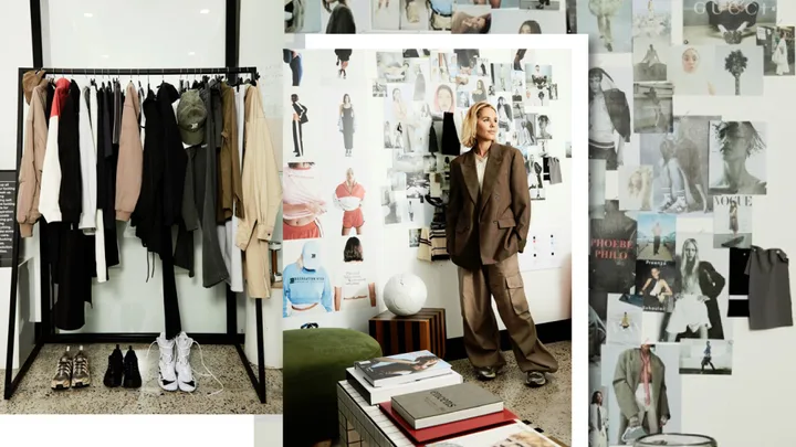 Fashion designer in oversized suit beside clothes rack and inspiration wall with fashion photos and books.