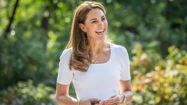 Kate middleton smiles while wearing a white, square-neck top