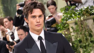 A person in a tuxedo at a formal event with photographers in the background.