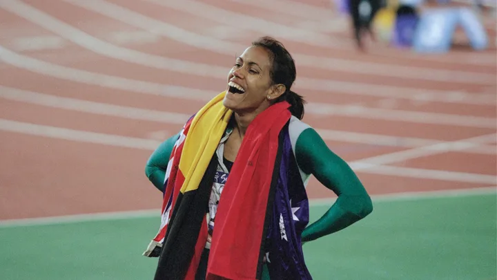 Cathy Freeman drapes the aboriginal and australian flags around her shoulders, smiling, at the 2000 sydney olympic games