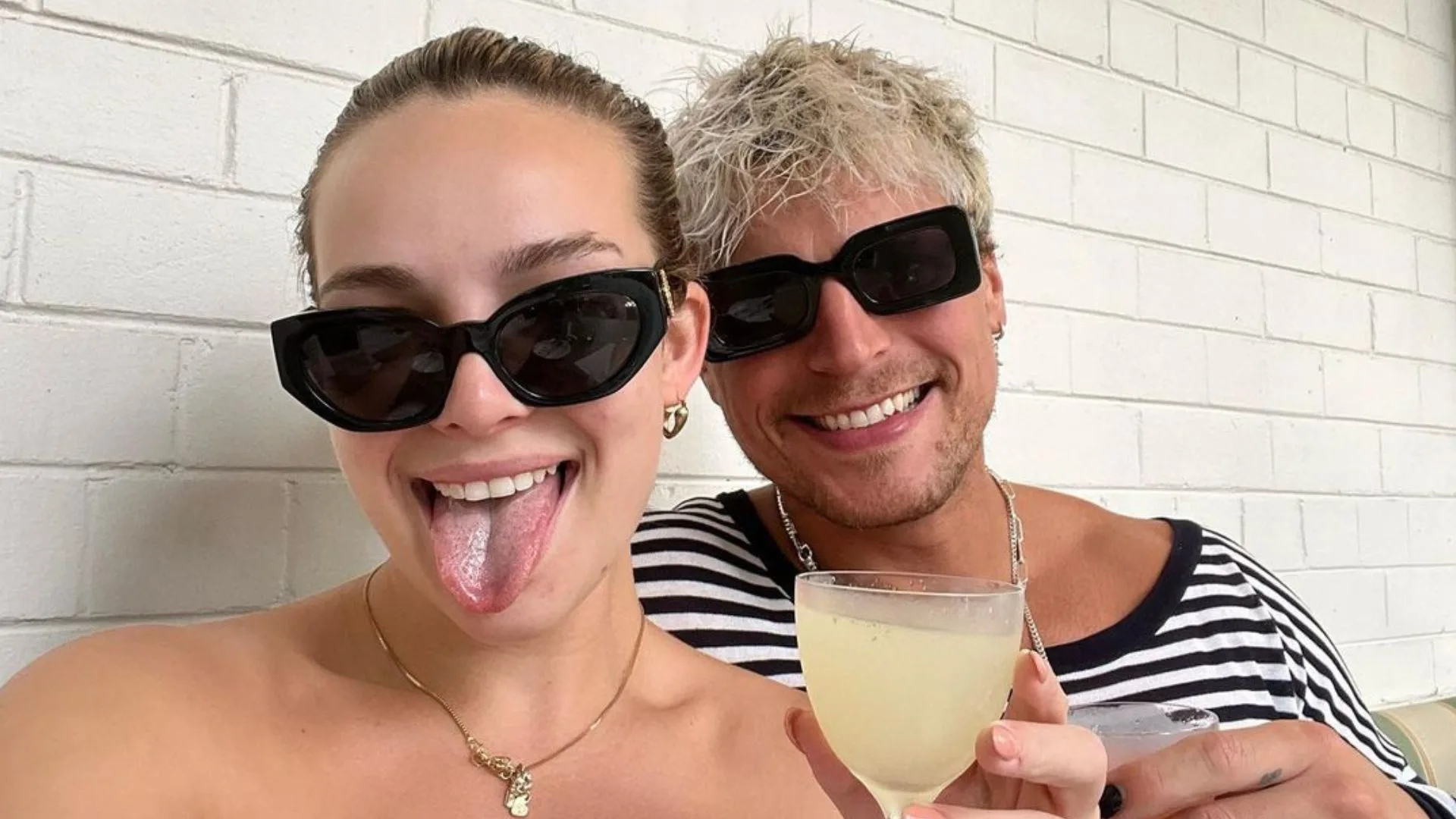 abbie chjatfield and her ex-boyfriend konrad bien-stephen wear sunglasses. Abbie holds a glass of wine and sticks her tongue out. Konrad wears a striped t shirt