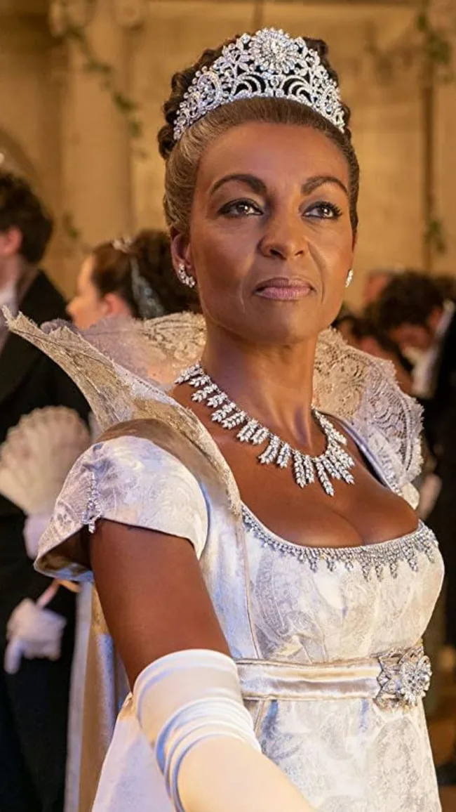 A woman wearing a sparkling tiara and ornate dress at a formal event, looking confidently to the side.