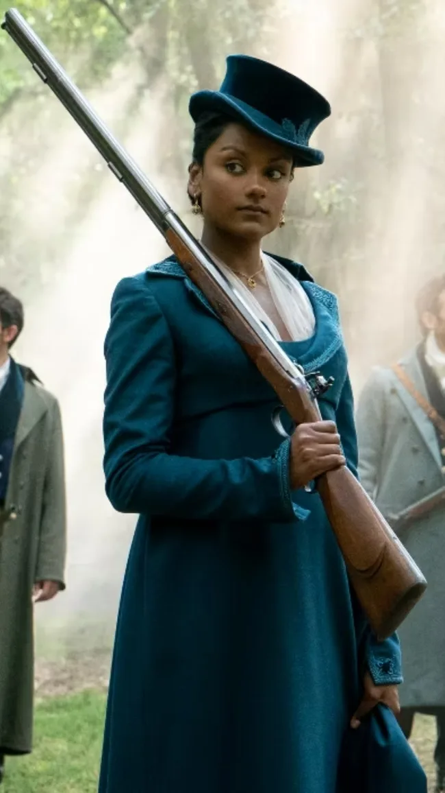 Woman in a blue dress and top hat holds a rifle in a misty forest setting.