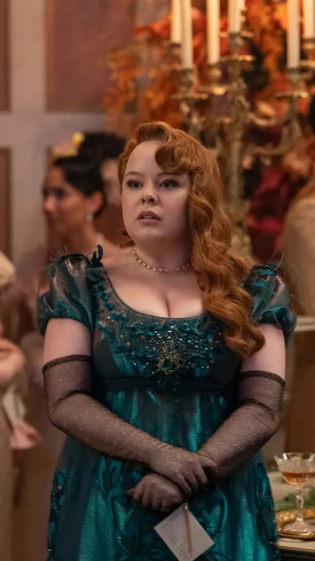 Woman in an elegant teal gown with long gloves at a formal event, standing in front of a candlelit background.