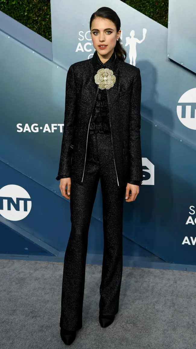 Person in a black suit with a large flower brooch stands on a SAG Awards red carpet.