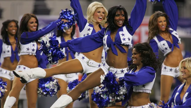Cheerleaders in blue and white outfits perform energetically with pom-poms at a sporting event.