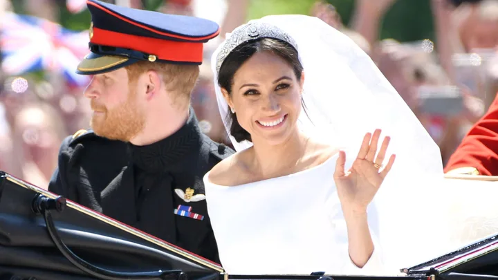 prince harry and meghan markle on their wedding day. The pair sit in a carriage and meghan waves at the camera