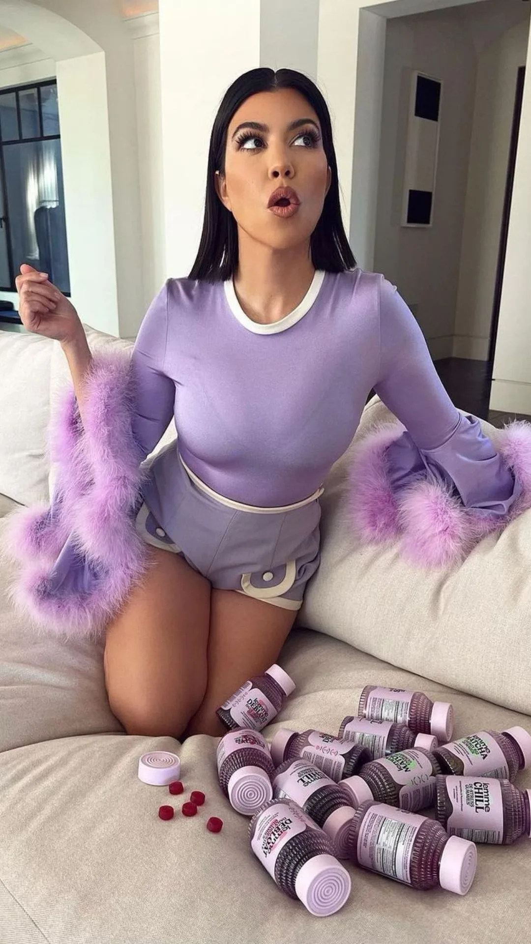 kourtney kardashian kneels on a couch next to bottles of vitamin gummies from her business Lemme