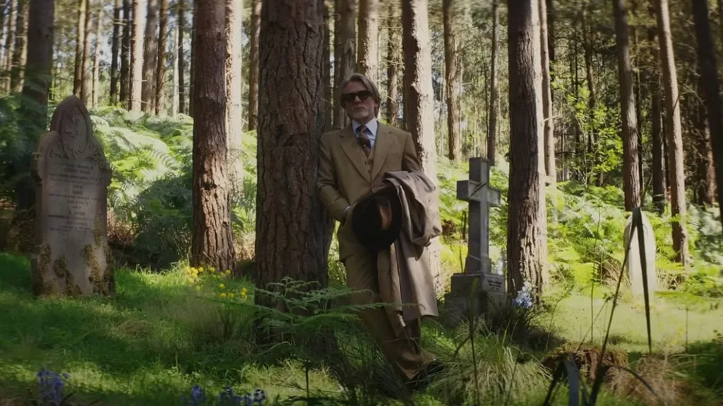 A man wearing a beige suit leaning against a tree in a forest.