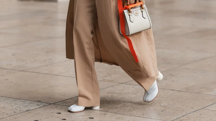 a photo of a woman's legs. She wears brown trousers, carries a white gucci bag and wears white margiela tabi boots