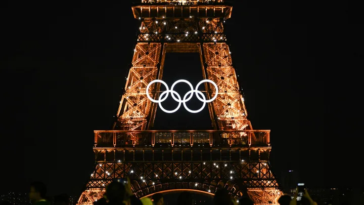 Eiffel Tower at night with illuminated Olympic rings displayed in front.