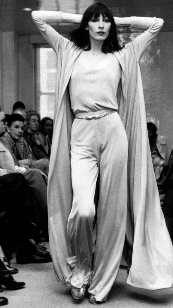 Angelica Huston wears a jersey evening pants ensemble and matching, full coat on a Halston Originals catwalk.