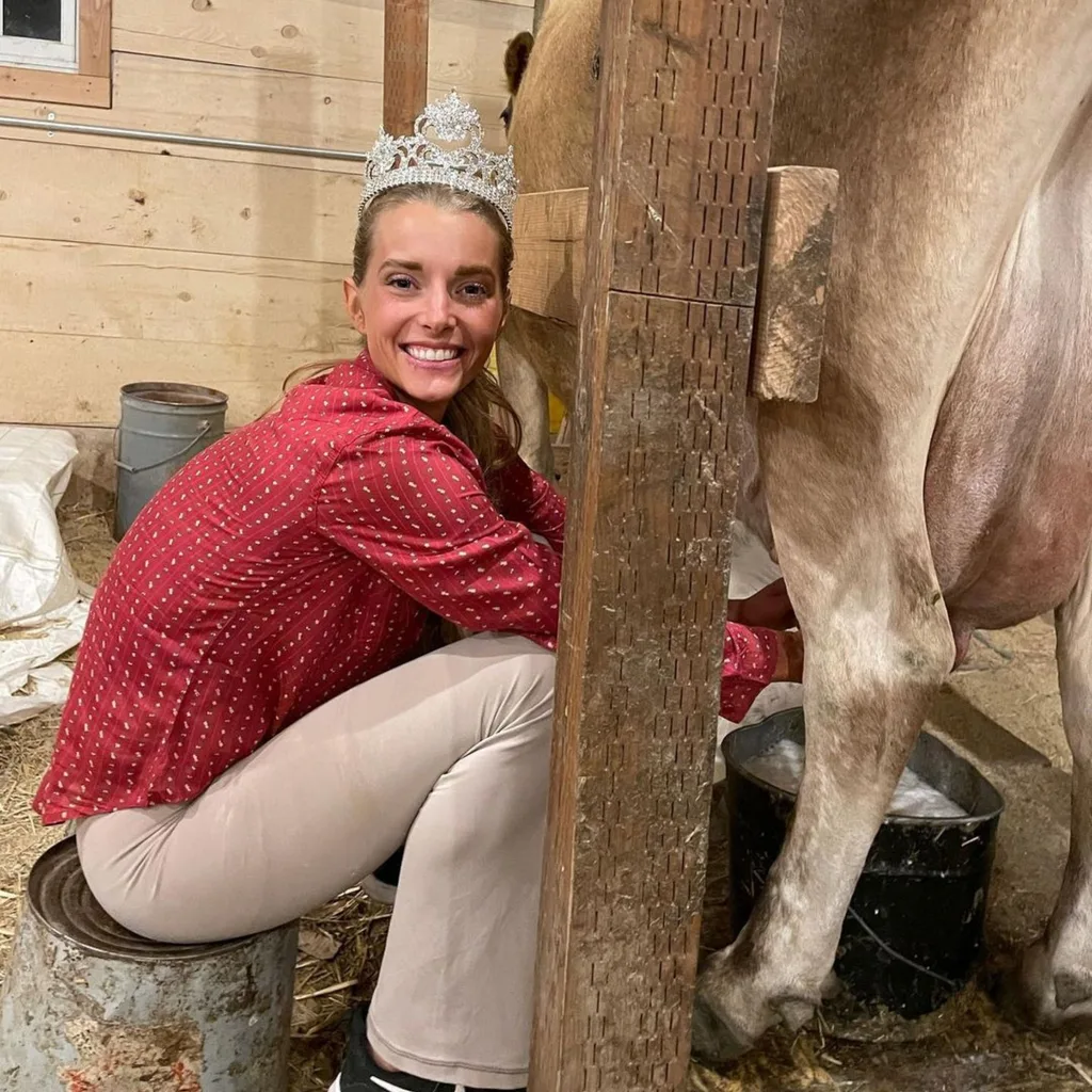 Hannah Neeleman, the influencer and "tradwife" who posts under Ballerina Farm poses milking a cow and wearing one of her pagaent tiaras. 