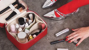 A woman with red stockings and silver heels packs her ultimate travel case for toiletries.