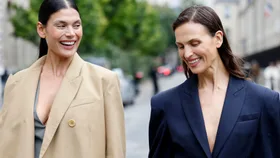 Two women walking together, smiling and holding hands outside at Paris Fashion Week