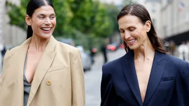 Two women walking together, smiling and holding hands outside at Paris Fashion Week