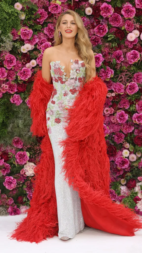 Blake Lively on the It Ends With Us red carpet wearing a floral column gown with a large feathered red cape. 