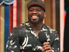 Curtis "50 Cent" Jackson speaks onstage during Day 3 of the 2024 Invest Fest at Georgia World Congress Center wearing a black baseball cap and a black and white graphic short sleeved shirt.