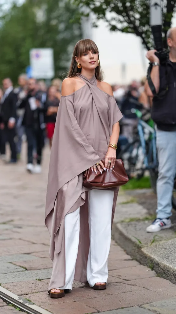 A woman wearing a light mauve long draped halterneck top and white pants outside at Milan Fashion Week.